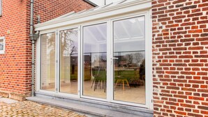 A modern house with a large glass door leading to a covered patio area. - Beautiful Mansion With Swimmingpool Close to Maastricht (Bilzen)
