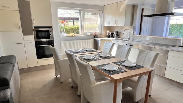 A modern kitchen with white cabinetry, a dining table set for four, and a large window providing natural light. - Lovely House in Heers With 2 Bedrooms (Heers)