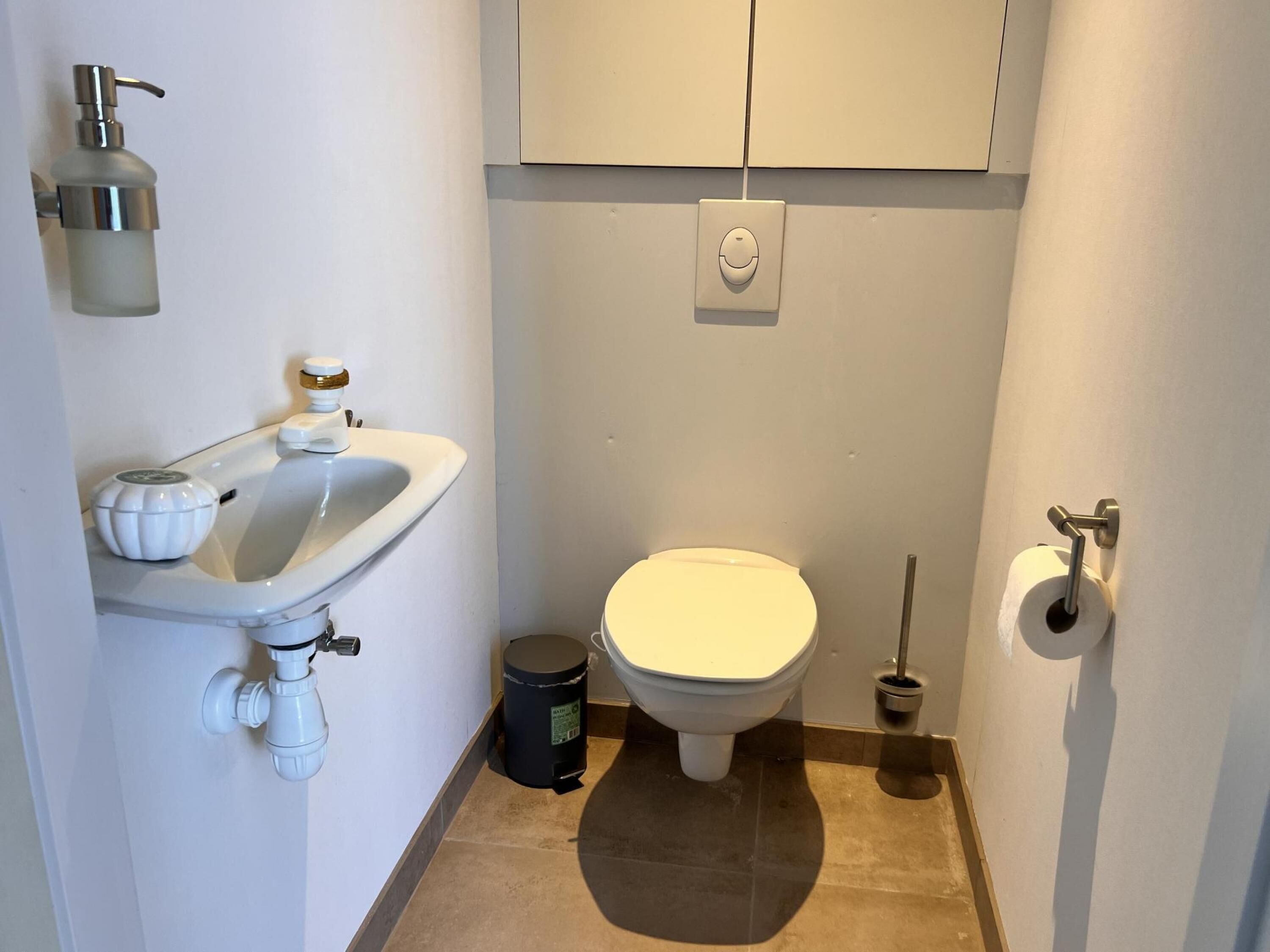 Pieni, siisti kylpyhuone, jossa on valkoinen pesuallas, wc ja roskakori.