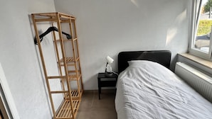 A bedroom with a bed, a wooden shelf unit, a small table with a lamp, and a radiator. - Lovely House in Heers With 2 Bedrooms (Heers)
