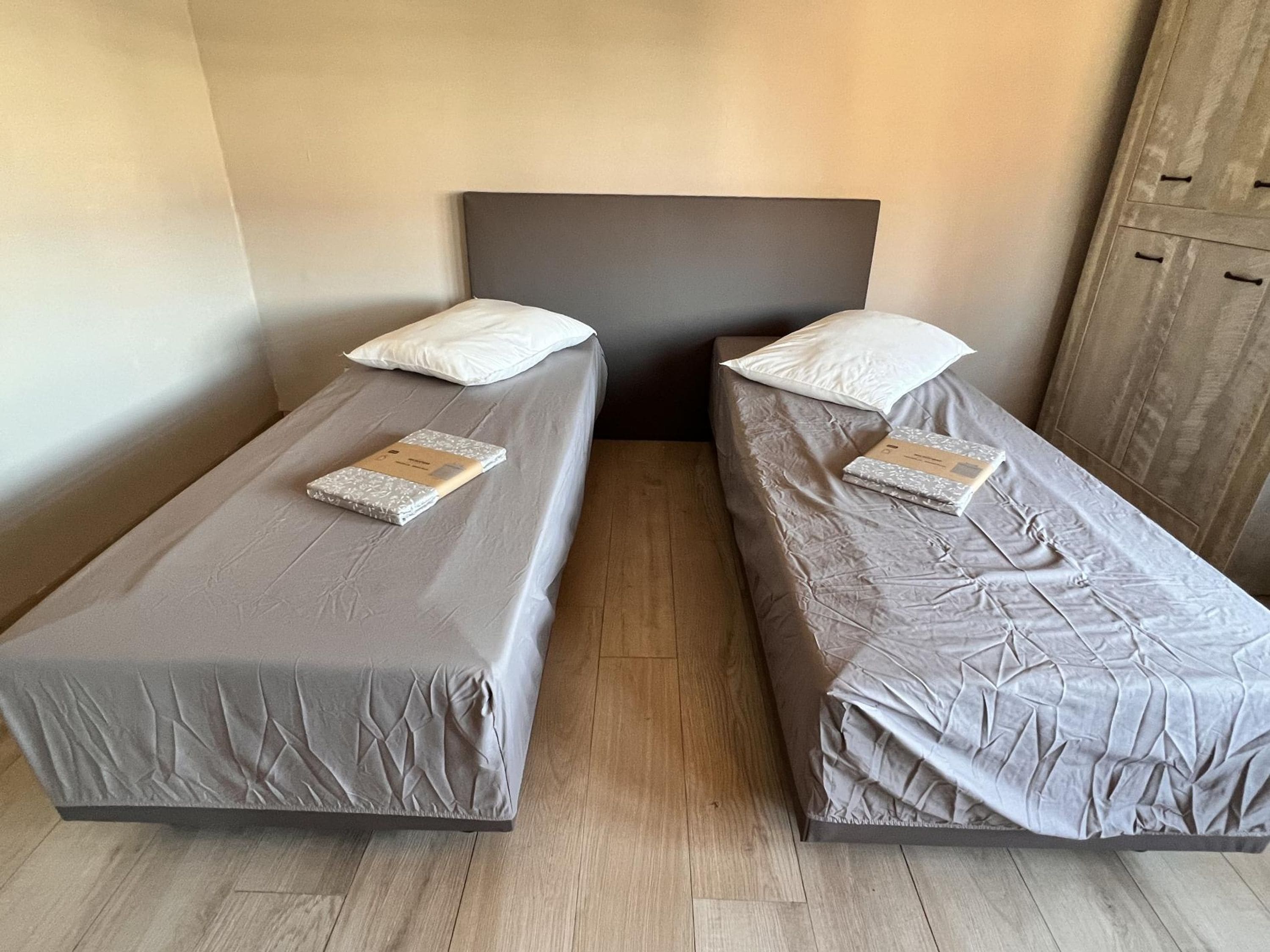 Two single beds with headboards, a wooden floor, and a wardrobe in the background.