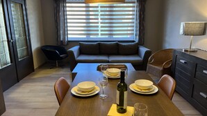 A dining area with a wooden table set for four, a sofa, and a window with blinds. - Beautiful House With 4 Bedrooms in Hees (Bilzen)