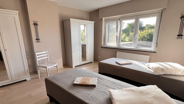 A bedroom with two beds, a white wardrobe, a chair, and a window with a view of greenery. - Beautiful House With 4 Bedrooms in Hees (Bilzen)