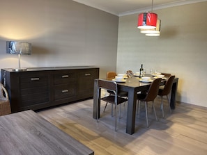 Zona pranzo moderna con tavolo in legno scuro, sei sedie e una lampada a sospensione rossa.