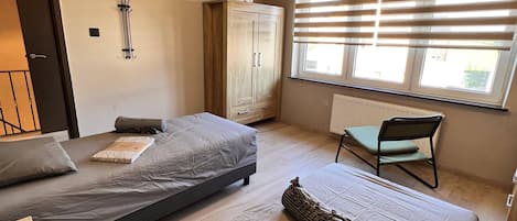 Un dormitorio con dos camas, un armario, una silla y un radiador.