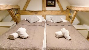 Una habitación con dos camas, vigas de madera, un cuadro pequeño en la pared y una lámpara a cada lado.