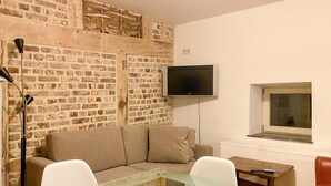 Una sala de estar con pared de ladrillo, un televisor de pantalla plana, un ventanal y una mesa de centro de vidrio.