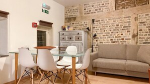 Un comedor con una mesa de vidrio y sillas blancas, un sofá gris y una pared de ladrillo.