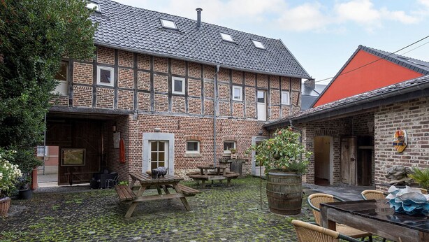 A courtyard with a cobblestone floor, wooden benches, and a table with chairs.
