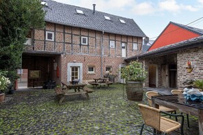 A courtyard with a cobblestone floor, wooden benches, and a table with chairs.