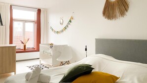A modern bedroom with a white crib, a grey headboard, and a bedside lamp. - Charming Retreat in the Heart of Oud-beijerland (Oud-Beijerland)