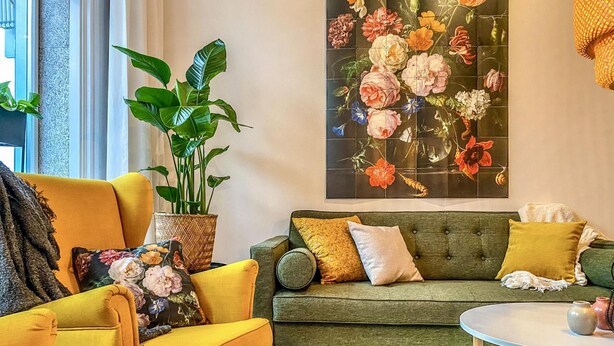 A living room with a yellow armchair, a green sofa, and a round coffee table. There is a large floral painting on the wall and a potted plant on the floor. - Charming Retreat in the Heart of Oud-beijerland (Oud-Beijerland)