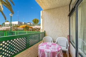 A balcony with a table and chairs, a green fence, and a building in the background.