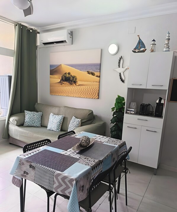 A modern living room with a sofa, dining table, and kitchen area.