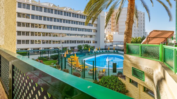 A hotel courtyard with a swimming pool, palm trees, and a multi-story building in the background.