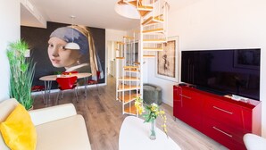 Una sala de estar moderna con una escalera espiral, un televisor grande y un comedor con sillas rojas.