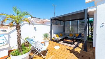Une terrasse sur le toit avec une plateforme en bois, un coin salon avec un canapé et des coussins, un palmier et une plante en pot.