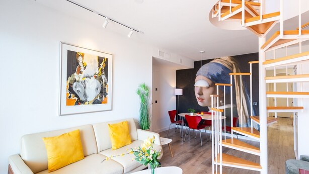 Una sala moderna con un sofá, una mesa de centro, un cuadro, una escalera y un comedor.
