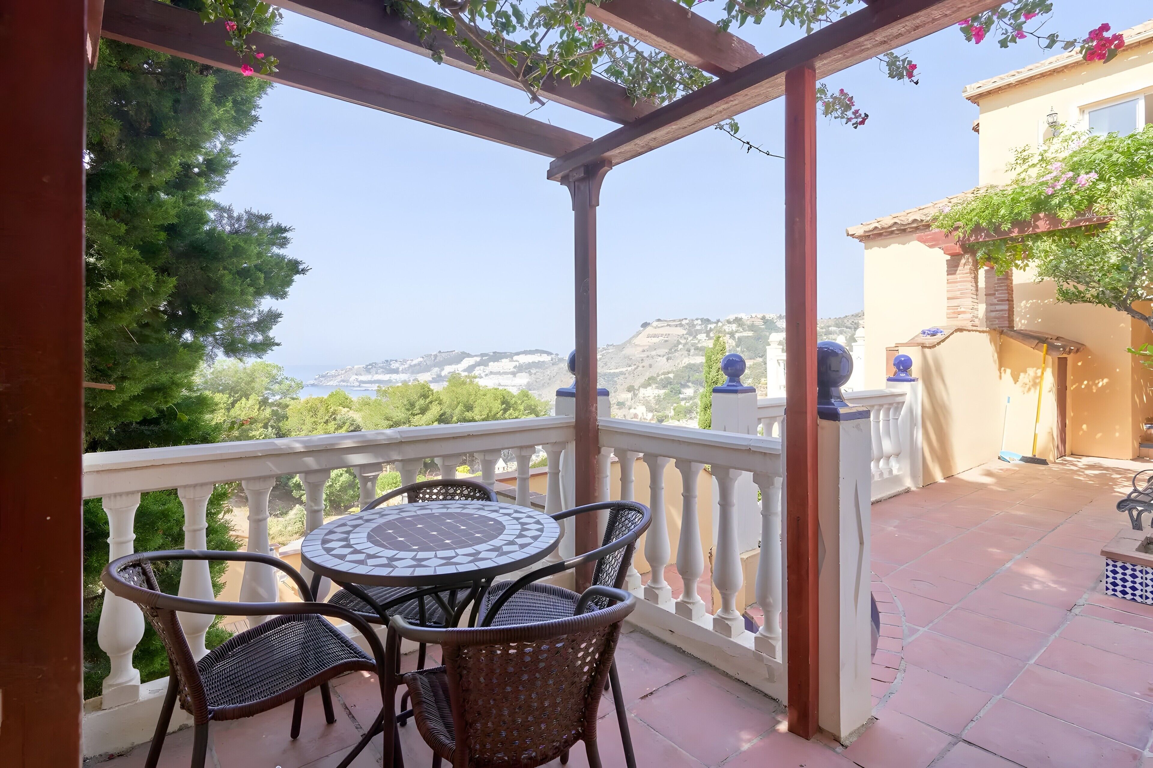 Un balcón con mesa y sillas, una pérgola y vistas al paisaje.