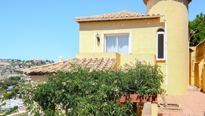 Un bâtiment jaune avec une tour, une fenêtre avec des rideaux et une vue sur une colline.