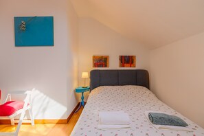 A bedroom with a bed, a nightstand, a lamp, a chair, and two paintings on the wall.