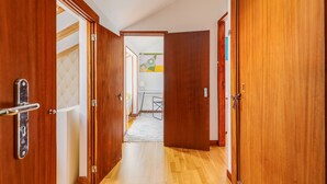 A hallway with wooden doors, a white ceiling, and a visible room with a bed and a desk. - Holiday Apartment "Atalaia Duplex" with Balcony & Wi-Fi (Lisboa)