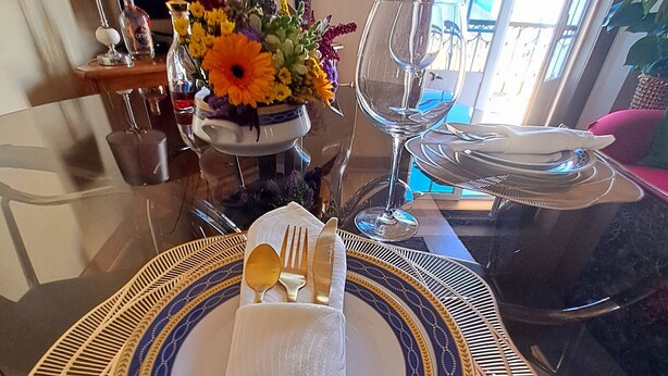 A dining table with a folded napkin, a glass of water, and a vase of flowers. - Holiday Apartment "Atalaia Duplex" with Balcony & Wi-Fi (Lisboa)