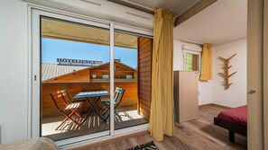 A hotel room with a sliding glass door leading to an outdoor seating area with a table and chairs. - Apartment for 6 people with mountain views, a swimming pool and parking (Allos)