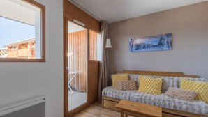 Ein gemütliches Zimmer mit einer Holzbank, einer Couch mit gemusterten Kissen, einem Gemälde einer verschneiten Landschaft und einer Glastür zu einem Außenbereich.