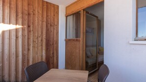 Eine Holzwand, eine Schiebetür aus Glas zu einem Schlafzimmer mit Bett und Kissen sowie ein Tisch mit Stühlen.