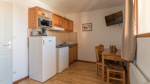 Eine kleine Küche mit Kühlschrank, Mikrowelle und Geschirrspüler, Holzschränken, einem Esstisch mit Stühlen sowie einem an der Wand montierten Fernseher.
