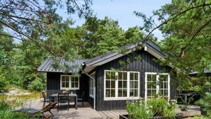 Une cabane en bois dotée d’une terrasse, entourée d’une végétation luxuriante et d’arbres.
