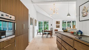 Une cuisine moderne avec des meubles en bois, un four encastré et un coin repas comprenant une table et des chaises.