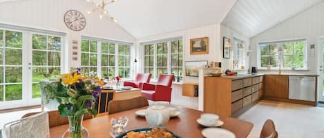 A spacious kitchen with a dining area, large windows, and a modern chandelier.