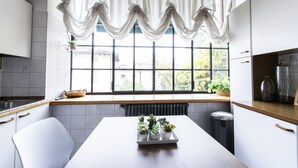 Una cocina moderna con armarios blancos, encimera de madera, una ventana con cortinas blancas y una mesa con plantas en macetas.