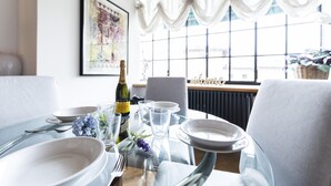 Una mesa de comedor dispuesta con platos blancos, copas, cubiertos, una botella de vino y un florero con flores.