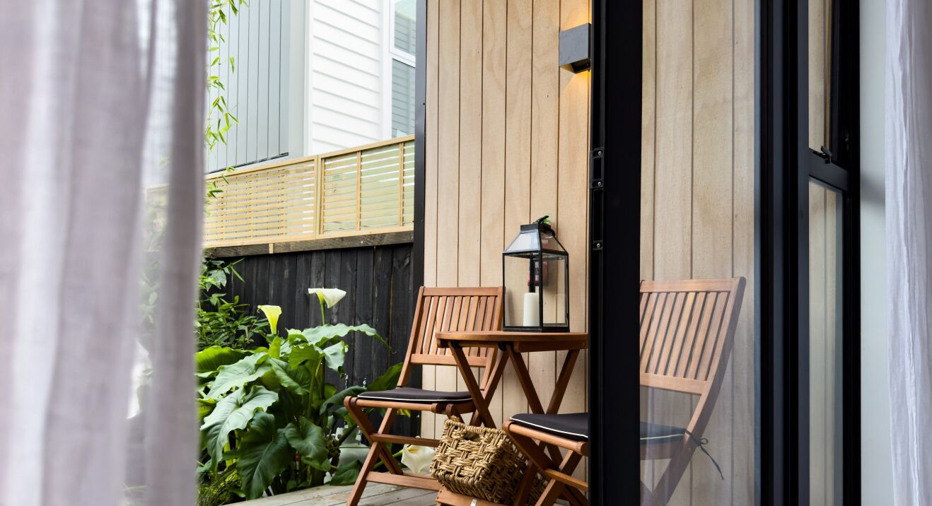 Une terrasse en bois avec deux chaises en bois et une table, un panier en osier et une lanterne fixée au mur.