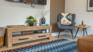 Una sala de estar moderna con un mueble de televisión de madera, un sillón gris, una mesita auxiliar y una alfombra estampada.
