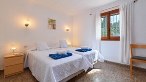 Une chambre avec deux lits, une table de chevet en bois, une chaise et une fenêtre avec des rideaux.