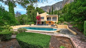 Une villa de style méditerranéen dotée d’une piscine, entourée d’une végétation luxuriante et avec des montagnes en toile de fond.
