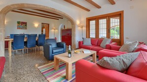 Un vaste espace de vie comprenant un canapé rouge, une table basse en bois et un coin repas avec des chaises bleues.