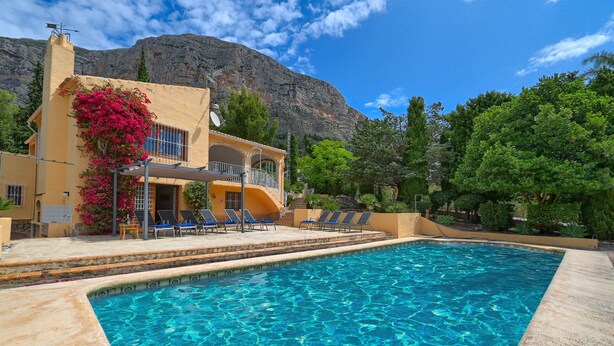 Une piscine à l’eau d’un bleu cristallin, entourée d’un bâtiment doté d’un balcon et de chaises longues.