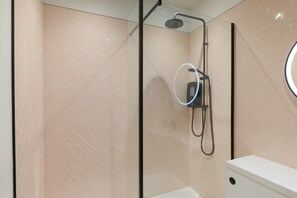 A modern shower enclosure with a glass door, a handheld showerhead, and a wall-mounted control panel.