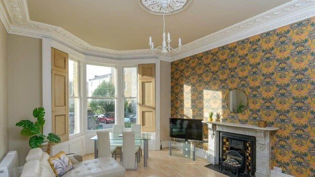 A living room with a large window, a fireplace, a television, and a sofa. - Gorgeous Apartment Seconds from Seafront, Clevedon (Clevedon)