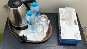 A stainless steel kettle, three water bottles, four glass cups, a tissue box, and a spoon on a wooden tray. - Cozy Central Room, Shared Bath & Kitchen (Abu Dhabi)