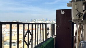 A balcony with a view of a cityscape, a green artificial turf, and a red plastic chair. - Cozy Central Room, Shared Bath & Kitchen (Abu Dhabi)