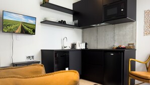 A modern kitchen with a built-in microwave, a coffee maker, and a refrigerator. There is a television mounted on the wall displaying a vineyard. - Gorgeous & Relaxing in Matakana (Matakana)