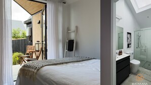 A bedroom with a large bed, a wooden chair, a radiator, and a sliding glass door leading to a balcony. - Gorgeous & Relaxing in Matakana (Matakana)