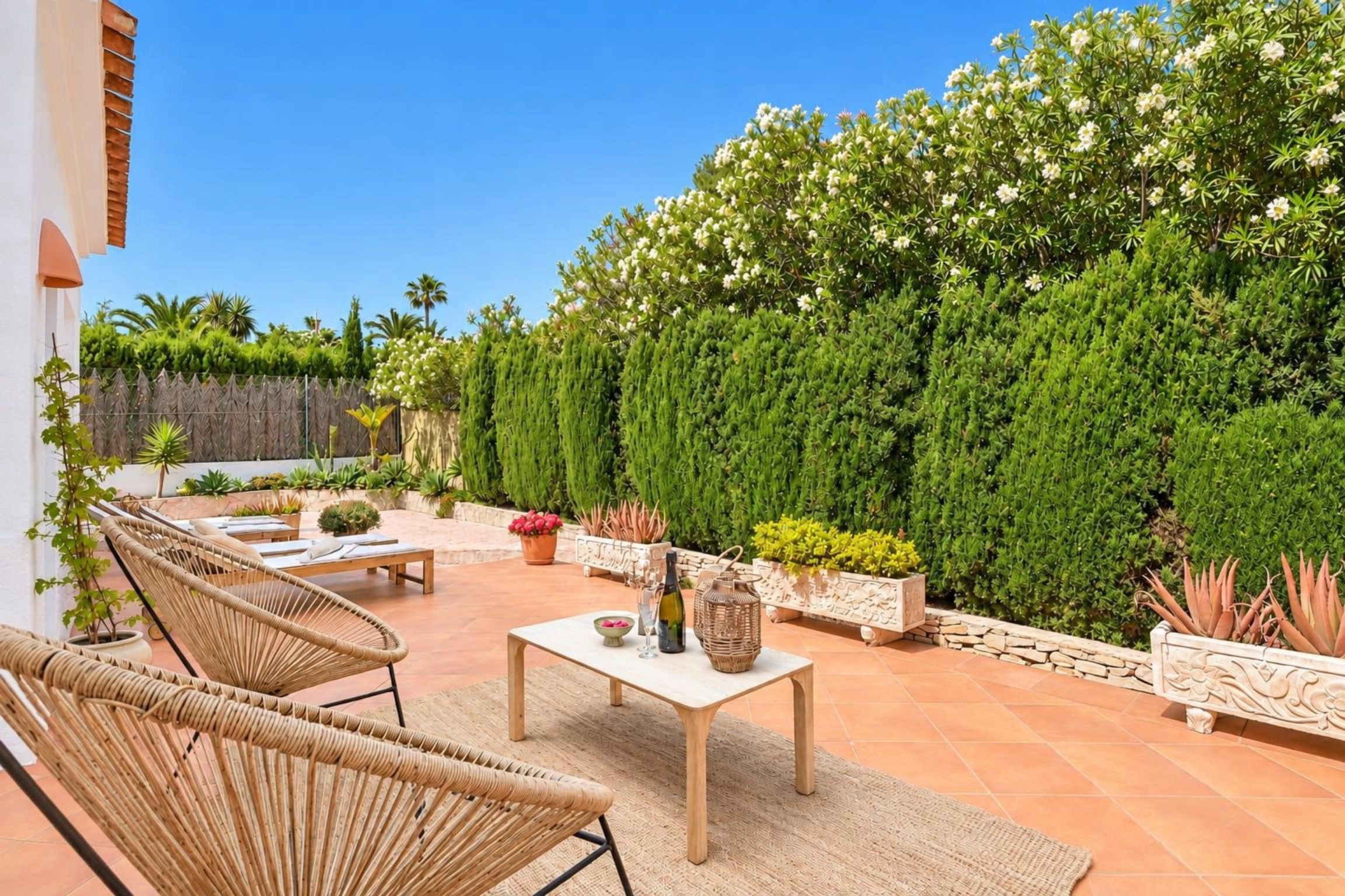 A patio with wicker furniture, a table with decorative items, and a variety of potted plants.
