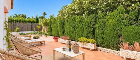 A patio with wicker furniture, a table with decorative items, and a variety of potted plants.